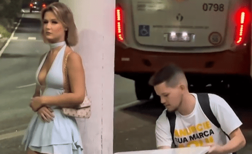 Homem organiza uma pequena mesa com flores, bebida e comida em uma rua tranquila durante a madrugada, convidando uma jovem para compartilhar um momento simples de conversa, respeito e conexão humana sob a luz dos postes.